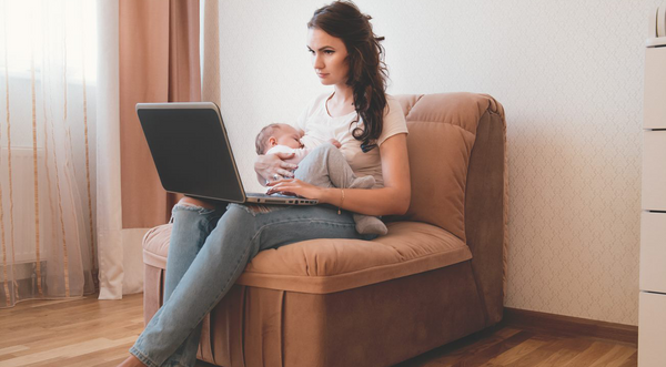 Woman breastfeeding while sitting down on couch and on a laptop