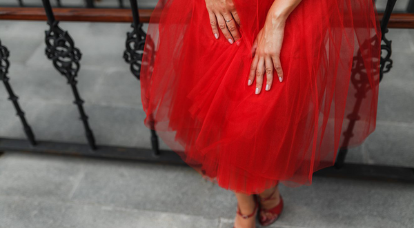 Woman wearing a long red fluffy dress leaning against a rail