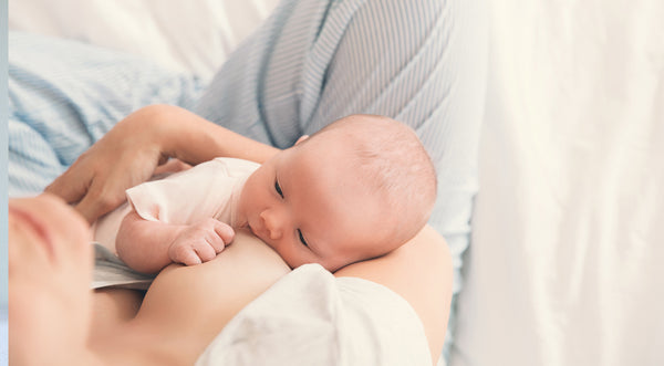Baby breastfeeding while mother sits with her legs crossed