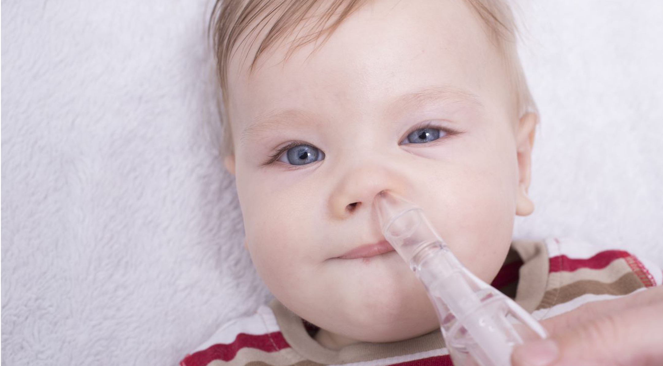 Baby lying down while mom uses a nasal aspirator in the babies nose